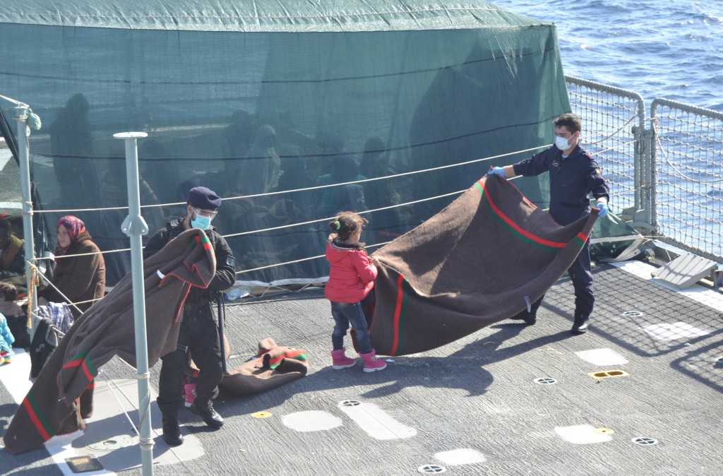 A little migrant girl helping a Portuguese sailor fold a blanket on the deck of Viana Do Castelo. November  15, 2014 Credit: Portuguese Navy