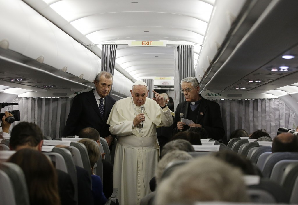 Pope Francis responding to reporters questions on the Papal Plane returning from Istanbul to Rome.  The priest standing next to him is his spokesman, Father Federico Lombardi. Photo for Mozzarella Mamma by AP Photographer Gregorio  Borgia. November 30, 2014.