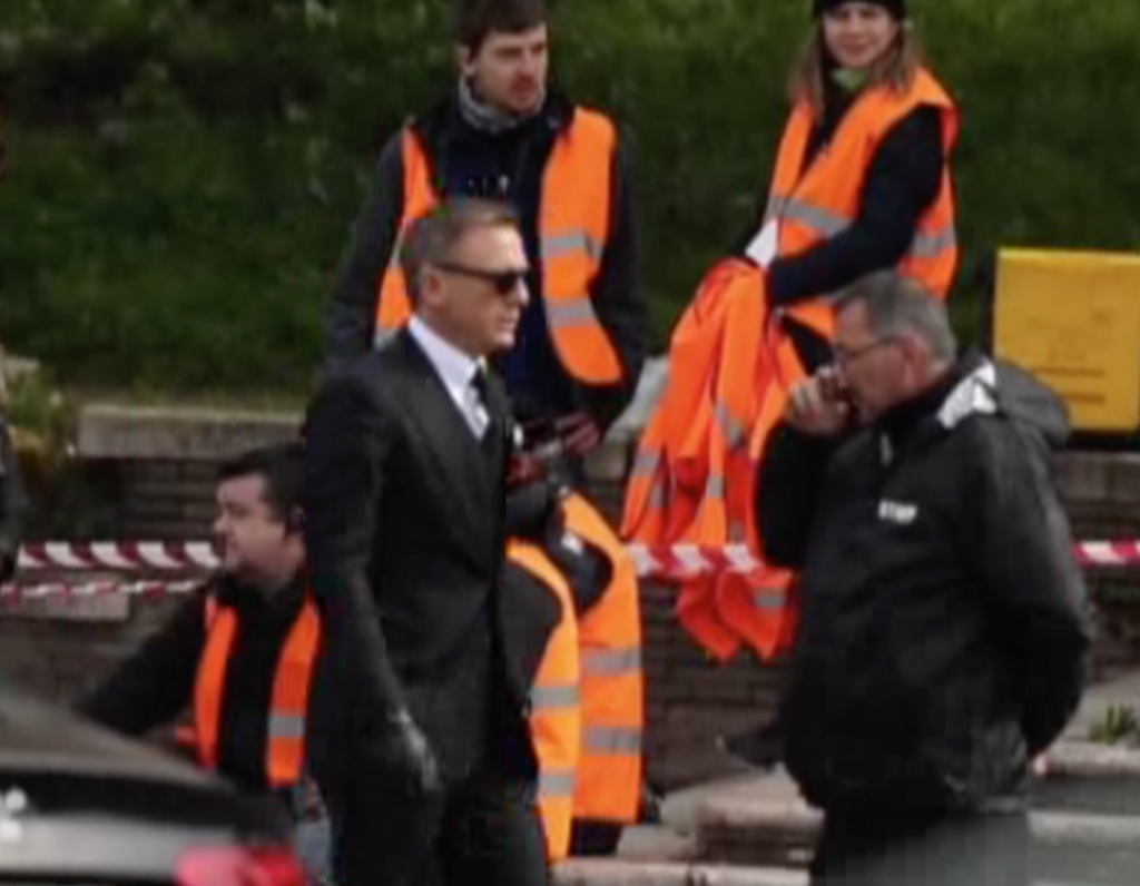 An impeccable Daniel Craig in black driving gloves working on a car chase scene and struggling with the cobblestones on Via San Gregorio in Rome. February 20, 2015