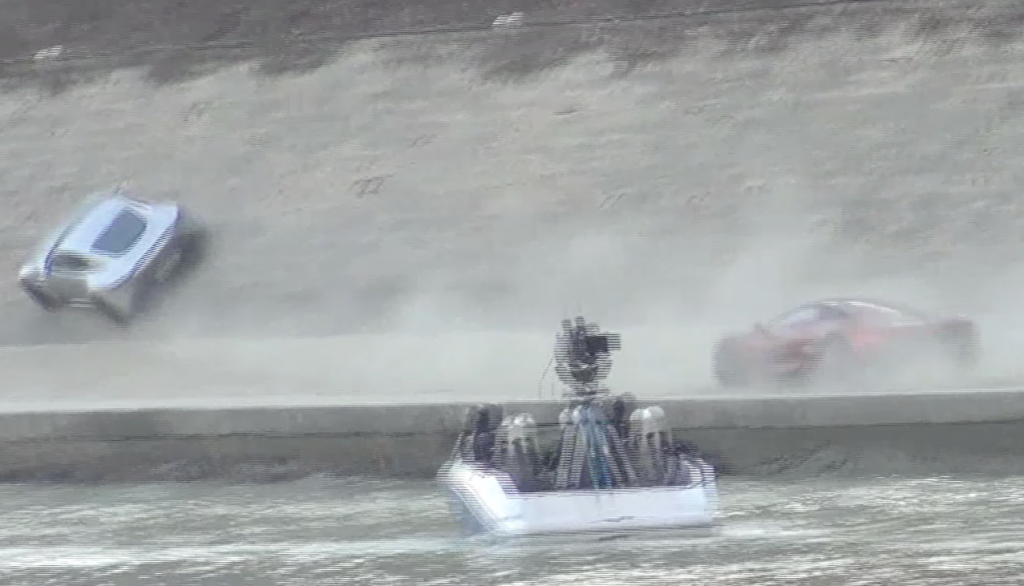 James Bond's Aston Martin drives up the embankment wall along the Tiber River in Rome with a jaguar racing along behind and cameraperson in helmets in boat.  February 20, 2015 (freeze frame of video from anonymous paparazzo camerawoman)