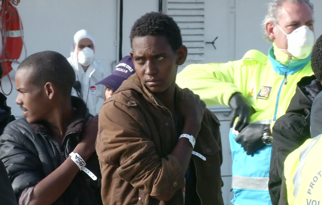 A young migrant stares forlornly off in the distance as he waits in line in the port of Pozzallo, Italy, shortly after disembarking from Italian Coast Guard ship after being rescued at sea. April 17, 2015. Freeze frame of video shot by AP Television Cameraman Luigi Navarra
