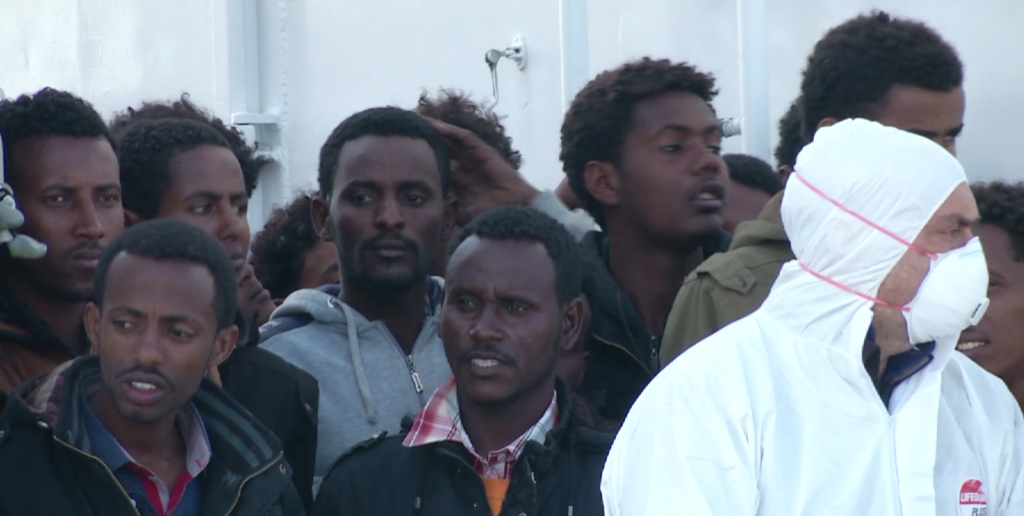 Migrants packed on the deck of a Coast Guard ship as it docks in port eagerly looking towards the shore. Freeze frame of video shot by AP Television Cameraman Luigi Navarra, April 17, 2015