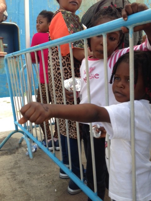 This little migrant girl proudly sticks her hand through a metal barrier in the port to show me the number 13 written in magic marker.  Photo by Trisha Thomas, May 5, 2015