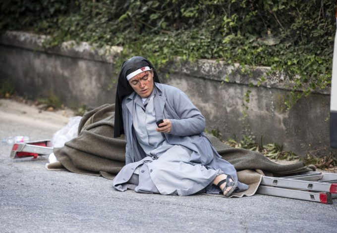Sister Marjana, from Albania, checks her mobile phone as she lies near a victim laid on a ladder following an earthquake in Amatrice Italy, Wednesday, Aug. 24, 2016. The magnitude 6 quake struck at 3:36 a.m. (0136 GMT) and was felt across a broad swath of central Italy, including Rome where residents of the capital felt a long swaying followed by aftershocks. (Massimo Percossi/ANSA via AP)