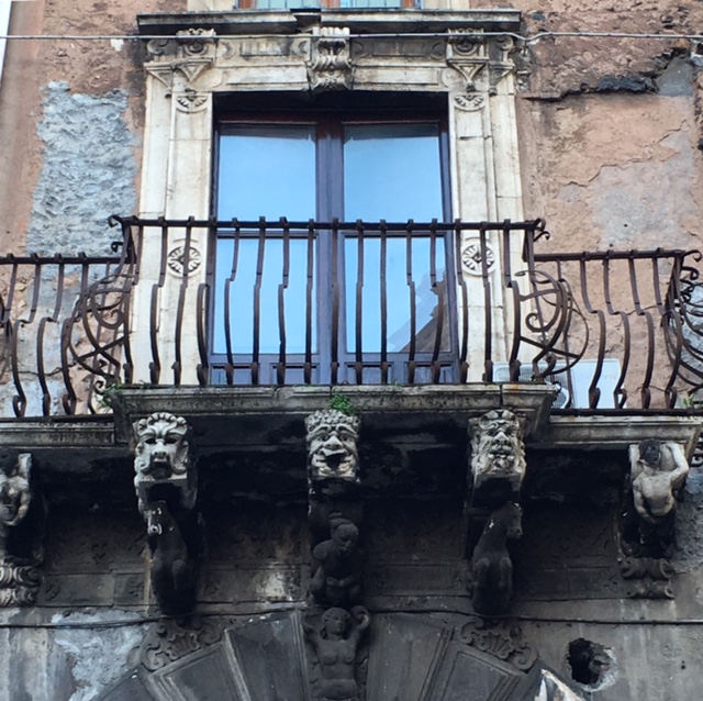 Balcony with funny baroque masks in Catania. Photo by Trisha Thomas, November 12, 2016