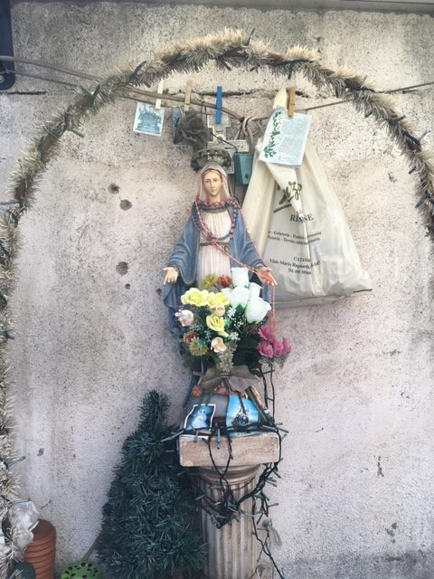 A Madonna with some Christmas lights and some plastic flowers at the corner of a parking lot in Catania, Sicily. Photo by Trisha Thomas, October 7, 2016