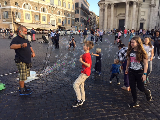 Children playing in bubbles blown by street performer in Piazza del Popolo, Rome, October 2017