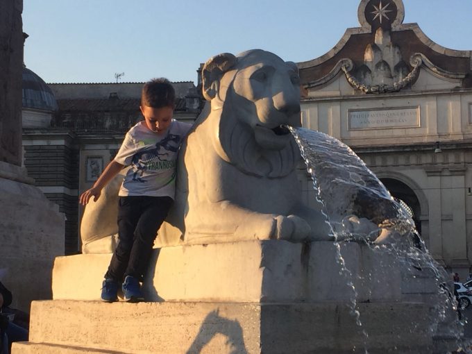 Boy playing on Lion Fountain at Piazza del Popolo, Rome. October, 2017